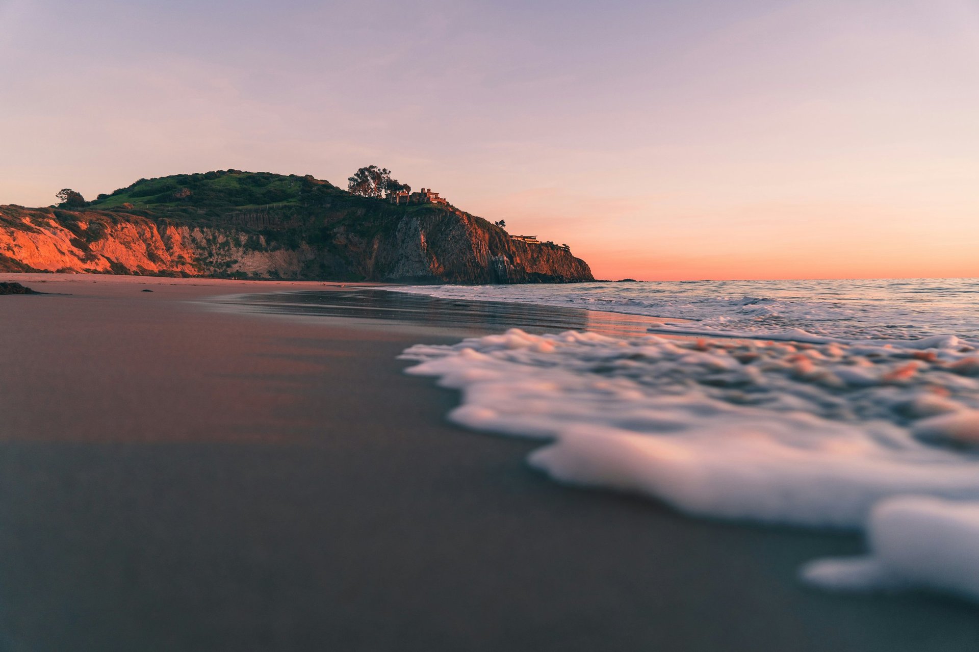 Sunset at a sandy beach with soft waves and a red sandstone cliff in the background under a golden sky