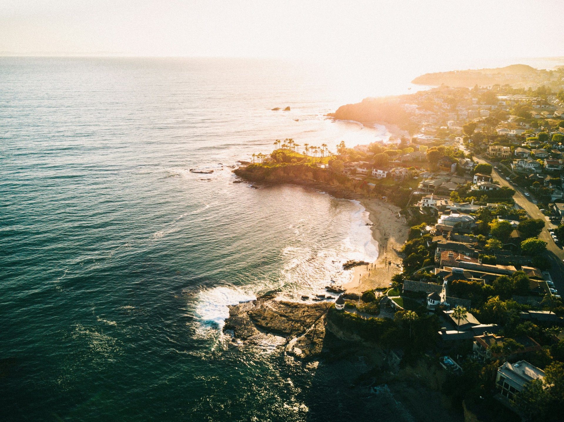 Aerial view of a rugged coastal landscape with turquoise ocean, rocky cliffs, and lush green vegetation at sunset